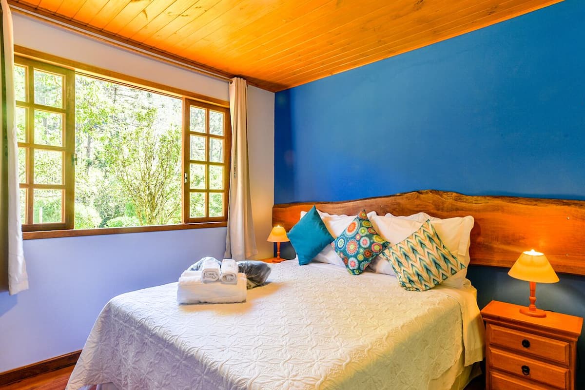 Une chambre à coucher avec un grand lit, une tête de lit en bois, une table de chevet avec une lampe et une fenêtre avec des rideaux.