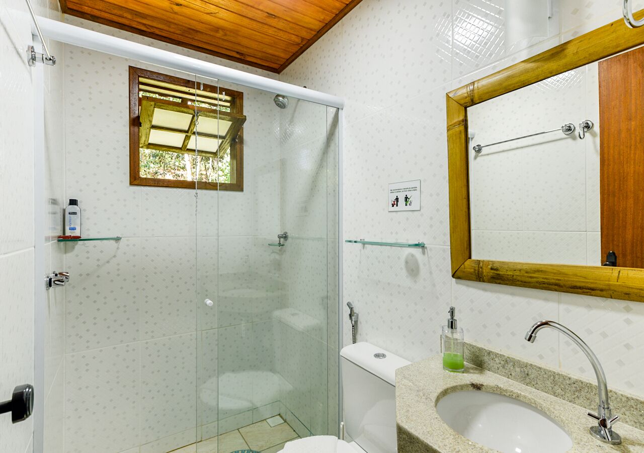 A bathroom with a glass-enclosed shower, a sink with a wooden frame mirror, and tiled walls.