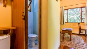 A compact bathroom with a toilet, a wooden door, and a window with curtains. - Amadamata Refúgio Ecológico (Nova Friburgo)