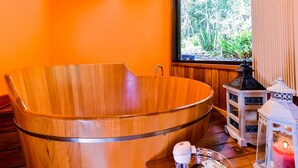 A wooden bathtub in a room with an orange wall, a window with a view of greenery, and two decorative lanterns. - Amadamata Refúgio Ecológico (Nova Friburgo)