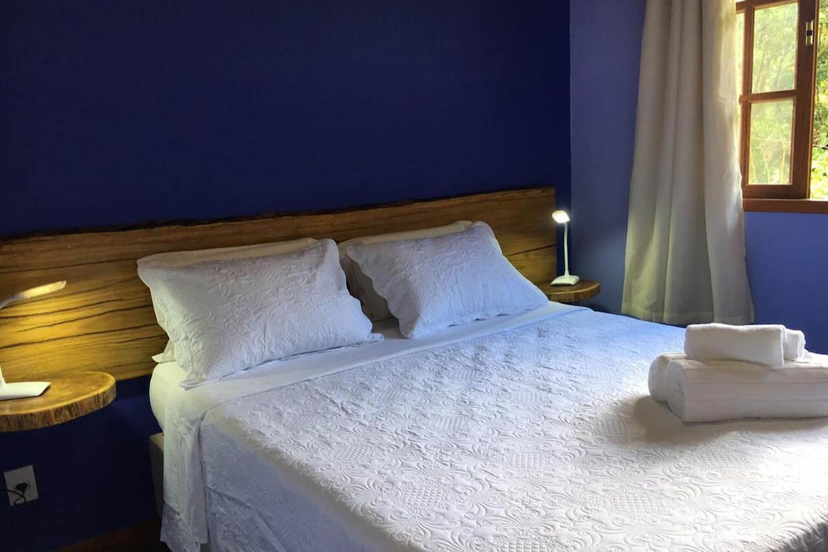 Un lit bien fait, avec du linge de lit blanc et des oreillers, une lampe de chevet et une fenêtre avec des rideaux.