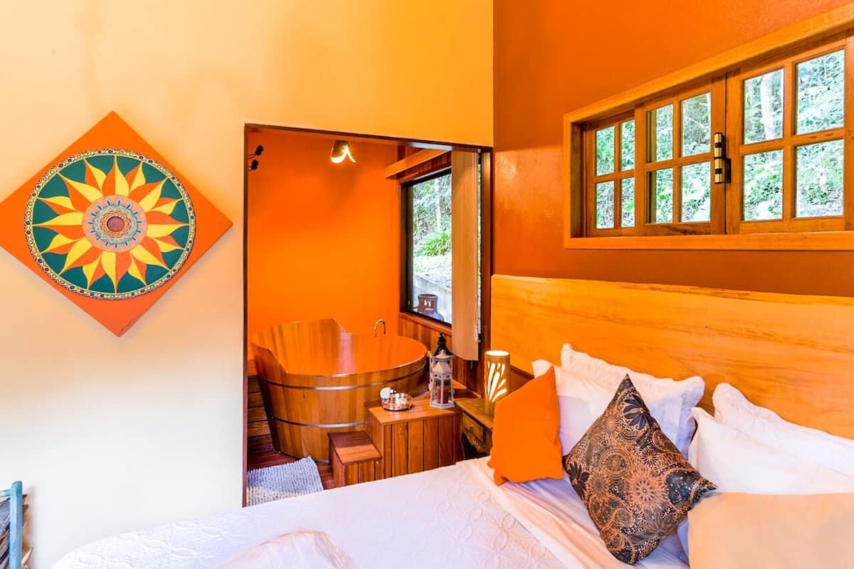 Une chambre avec un lit, une baignoire en bois et une fenêtre donnant sur la forêt.