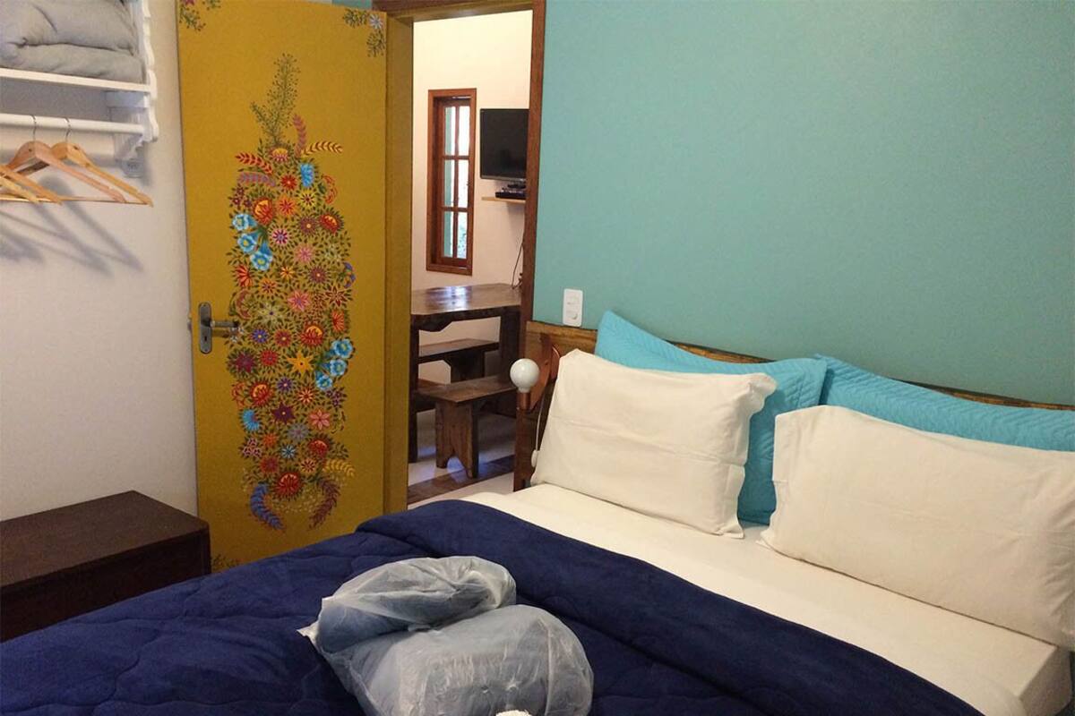 Une chambre à coucher comprenant un lit, des oreillers, une table de chevet en bois, une chaise, un téléviseur et une porte ornée de motifs floraux.
