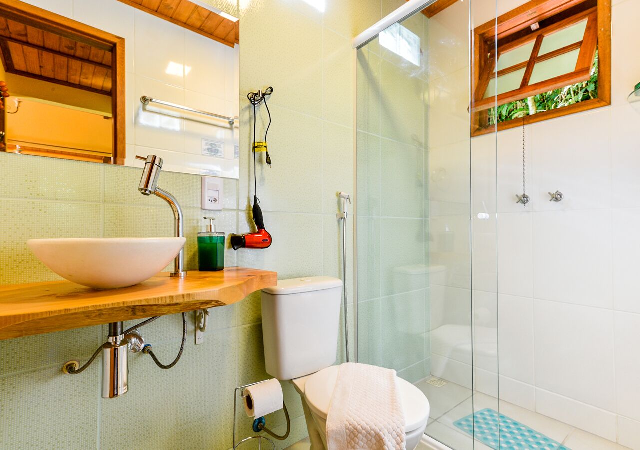 Une salle de bain avec un meuble-lavabo en bois, un lavabo blanc, des toilettes et une douche à parois de verre.