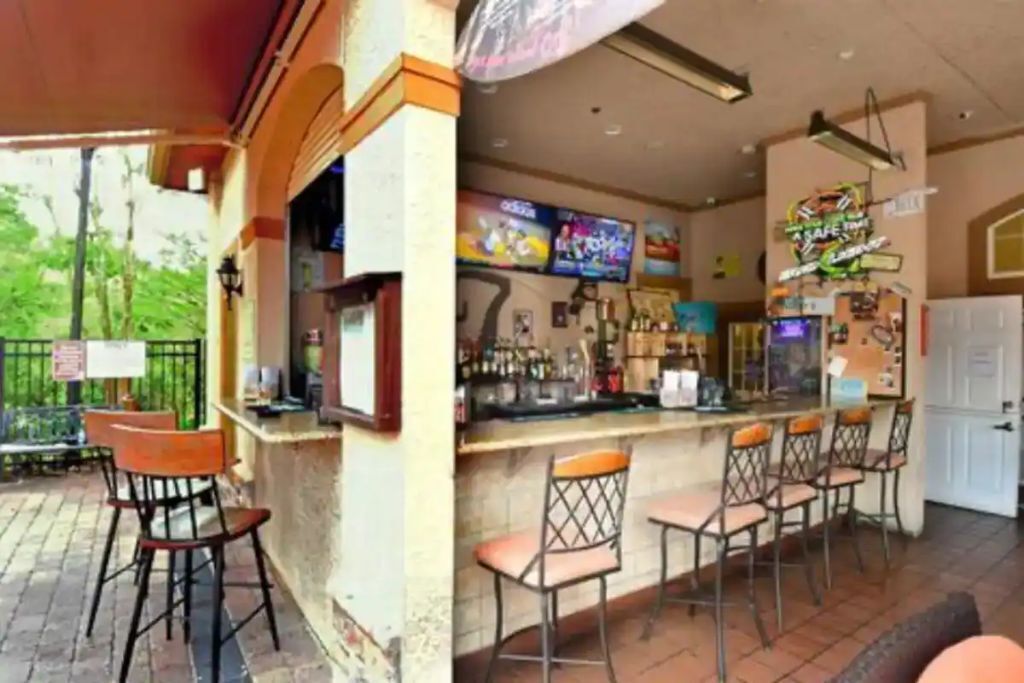 An outdoor bar area with a counter, multiple bar stools, and a variety of bottles and glasses.