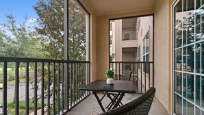 A balcony with a table and chairs, a potted plant, and a view of a building and trees. - Near Disney/Resort Pool, Bar & Gym (Davenport)