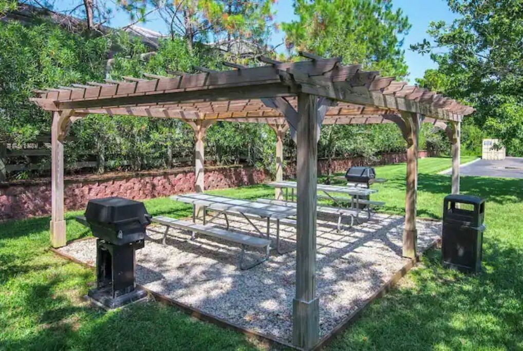 Une pergola en bois avec des tables de pique-nique et un barbecue.