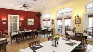 Un espace repas comprenant plusieurs tables et chaises, un ventilateur de plafond et un mur rouge orné de tableaux.