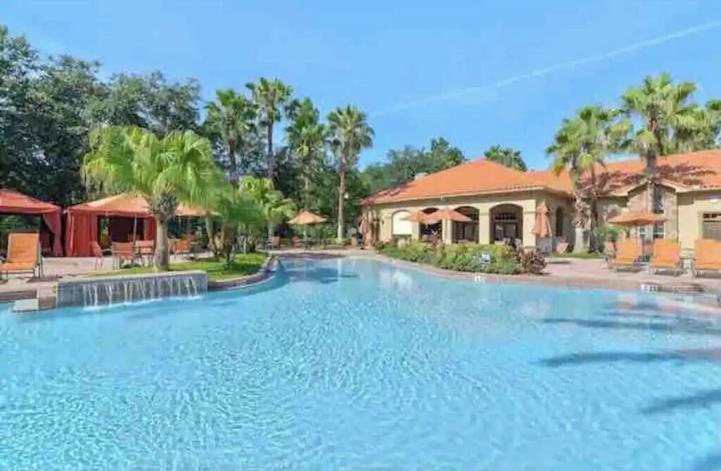 A swimming pool with a water feature, surrounded by palm trees and covered seating areas.