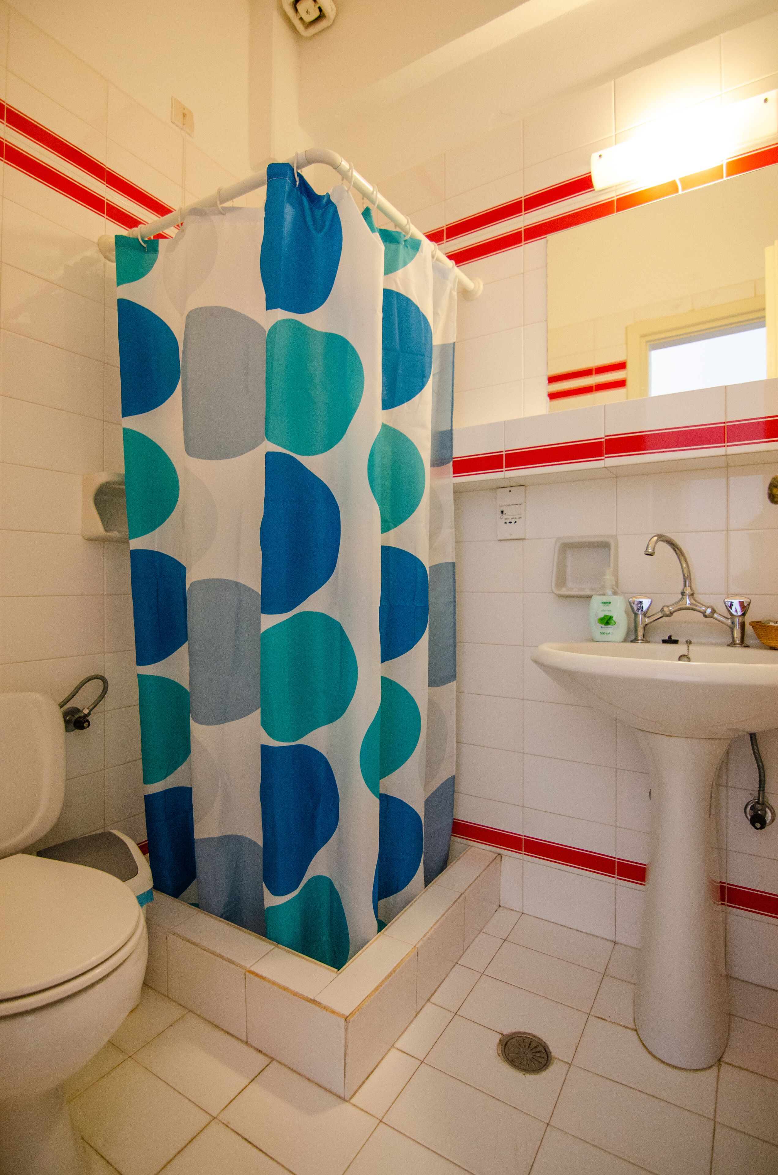 Une salle de bain avec un rideau de douche, des toilettes, un lavabo et des murs carrelés.