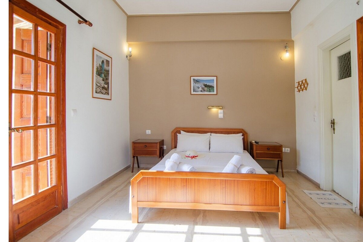 A bedroom with a wooden bed, two bedside tables, a nightstand, and a large window with a view.