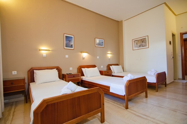 A hotel room with three wooden beds, each with a nightstand and a lamp.