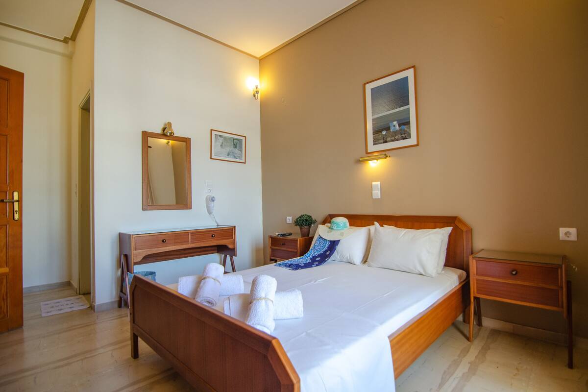 Une chambre d’hôtel avec un lit en bois, une table de chevet, une commode, un miroir et un tableau accroché au mur.