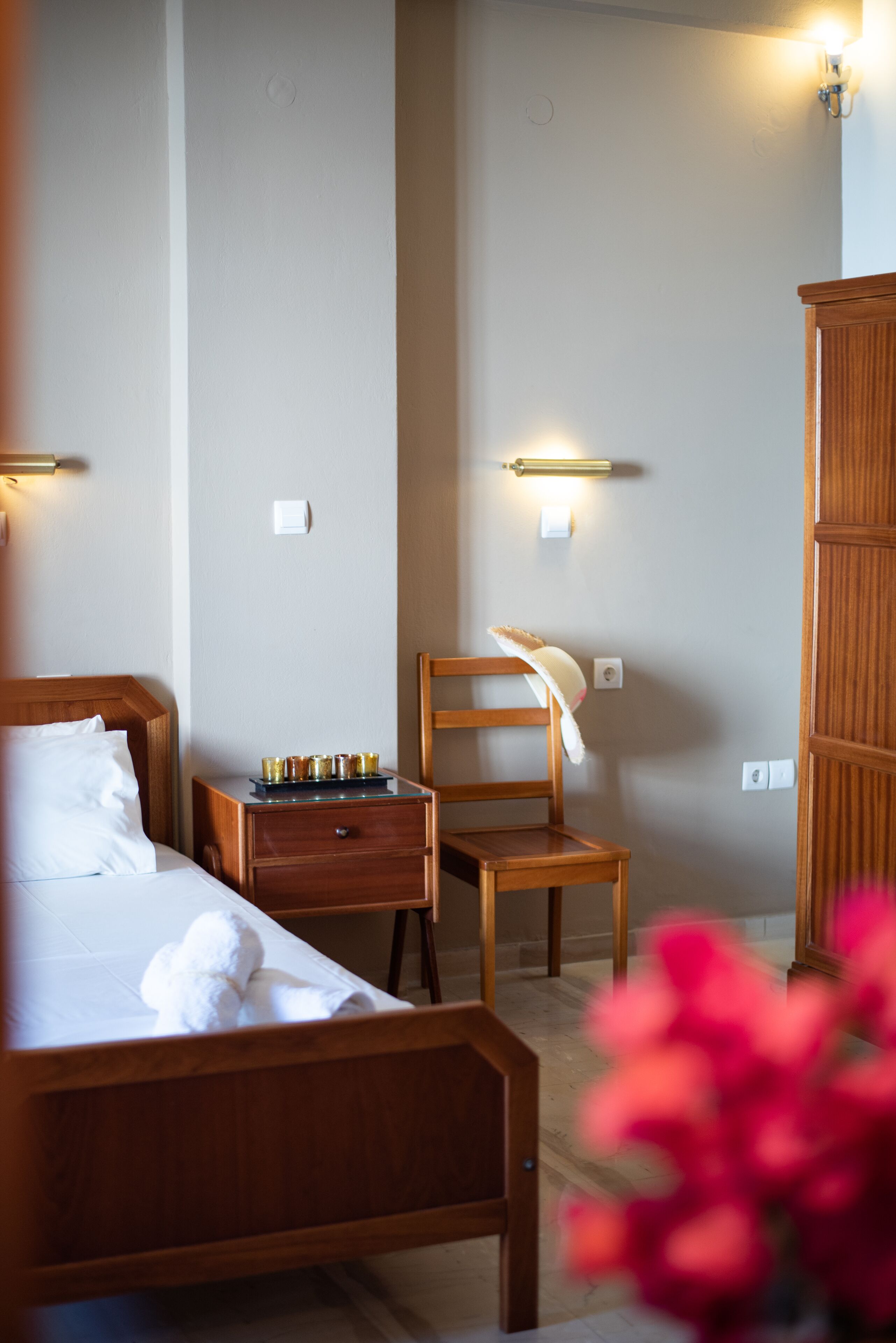 Habitación de hotel con cama de madera, una mesita de noche con bandeja de velas, una silla de madera y un armario.