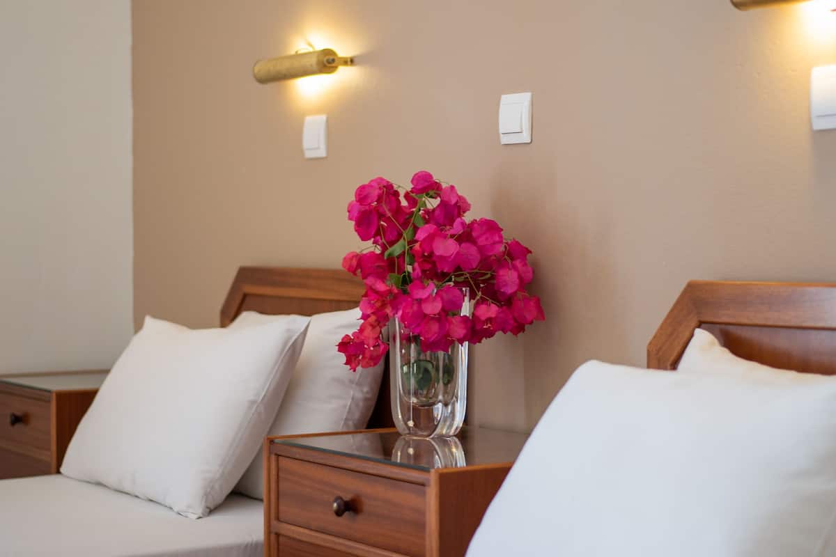 Une chambre d’hôtel avec deux lits, une table de chevet ornée d’un vase de fleurs roses et un tableau encadré accroché au mur.
