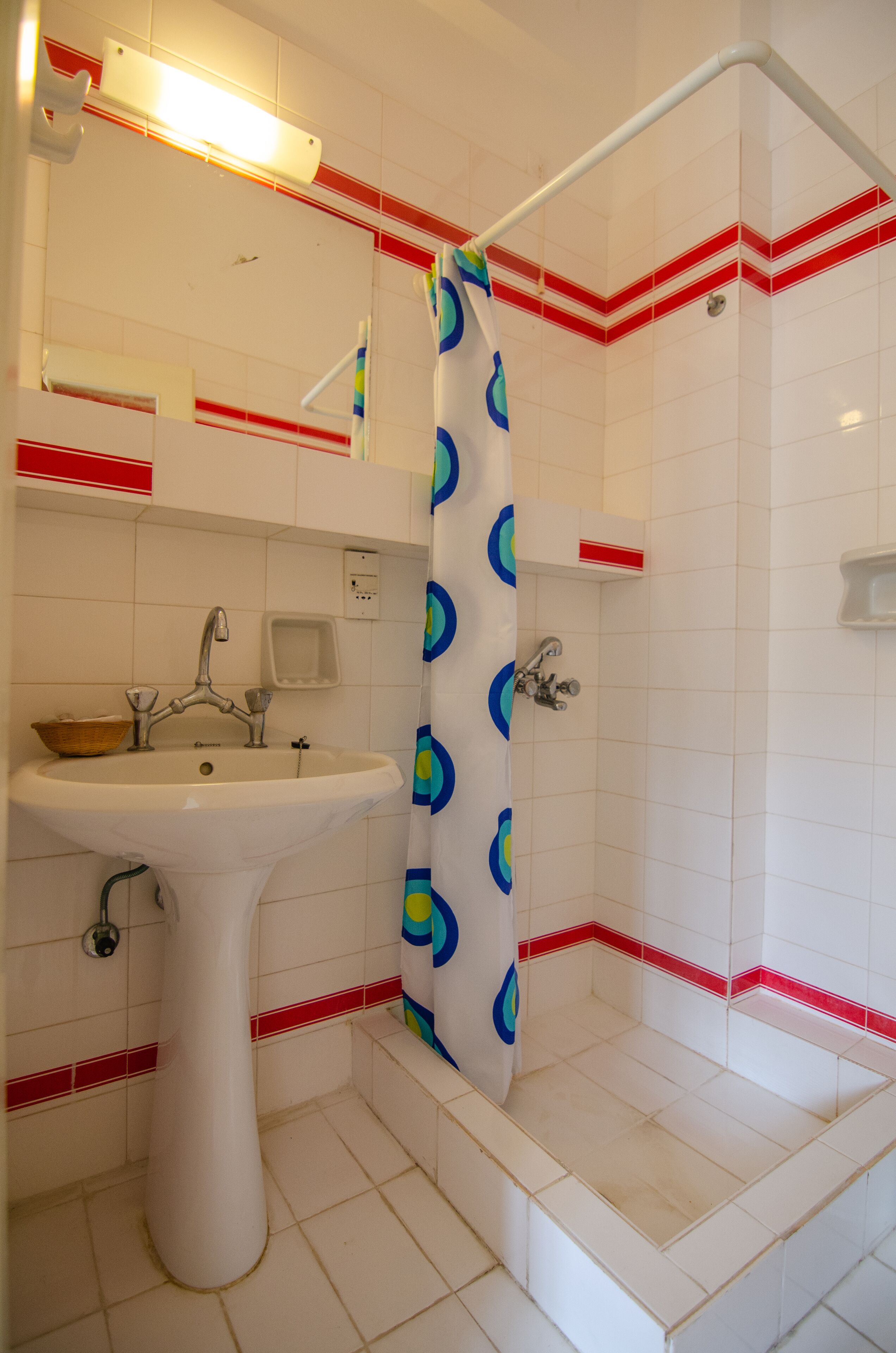 A bathroom with a white sink, a shower with a blue and green shower curtain, and red and white tiled walls.
