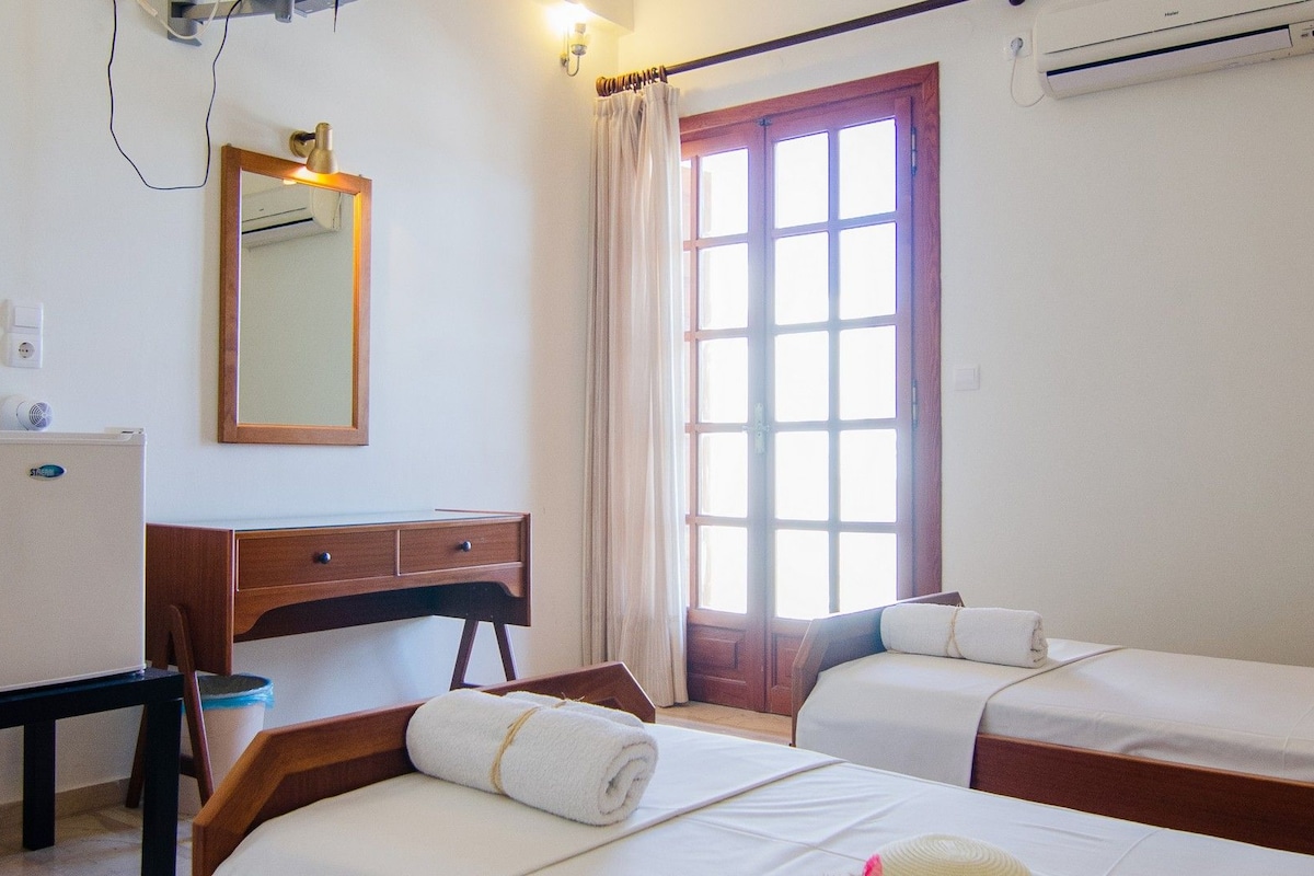 Una habitación de hotel con dos camas, un escritorio, un espejo y una ventana con cortinas.