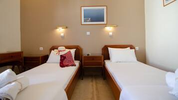 A hotel room with two single beds, a desk, and a nightstand. There is a framed picture on the wall and wall-mounted lights.