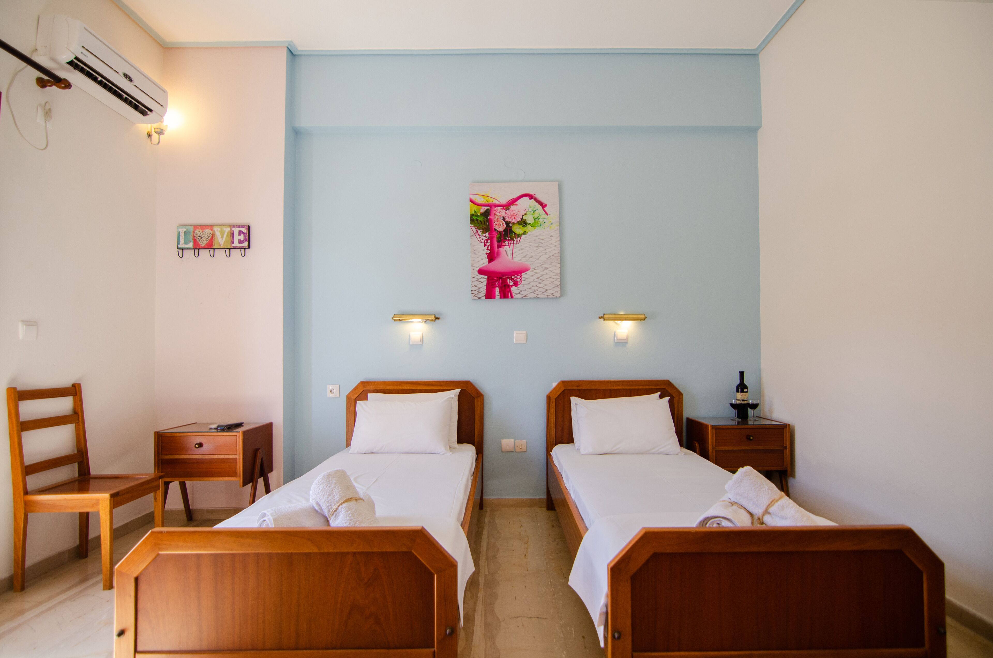 A room with two wooden beds, a desk, a chair, a wall-mounted air conditioner, and a wall decoration.