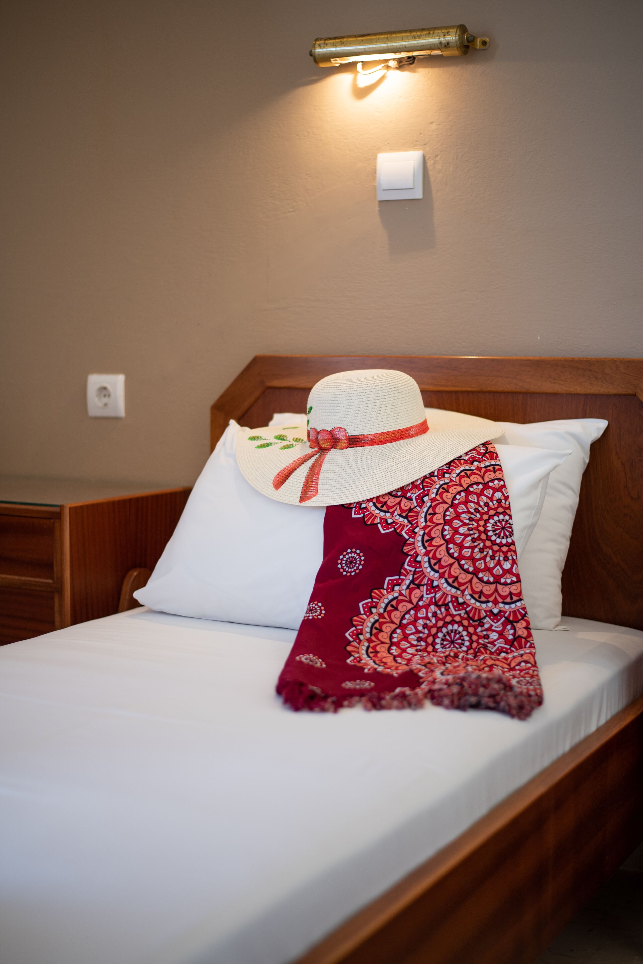 Un lit bien fait, avec un drap blanc, un plaid rouge à motifs et un oreiller blanc orné d’un nœud rouge.
