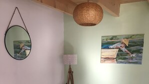 Una sala de estar con un sofá marrón, una mesa de centro redonda, una lámpara de pie, un espejo montado en la pared y un cuadro de un niño junto a un lago.