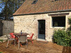 A stone building with a tiled roof, a wooden deck, and outdoor seating.