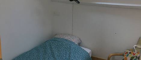 Ett litet rum med en enkel säng, ett takfönster, en stol och ett eluttag på väggen.