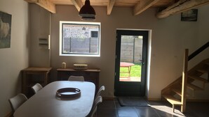 Un comedor con una mesa, sillas, una lámpara colgante, un ventanal con vistas al exterior y una escalera de madera.