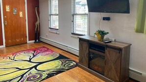 Un salon doté d’un plancher en bois, d’un tapis aux couleurs vives, d’un téléviseur fixé au mur et d’une cheminée.