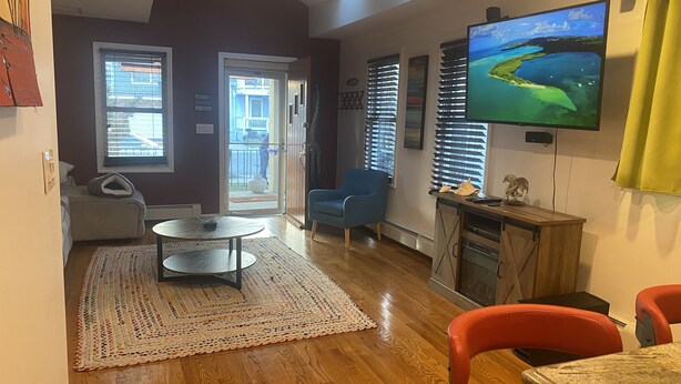 Un salon équipé d’un téléviseur et d’un ventilateur de plafond, d’un coin repas avec une table et des chaises, et offrant une vue sur l’extérieur grâce à une porte.