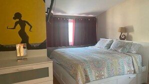 Une chambre à coucher comprenant un lit, une commode, un miroir, une lampe et un mur orné d’une silhouette.