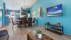 A modern kitchen with dark cabinets, a dining area with wooden chairs, a large TV on the wall, and a potted plant on the floor. - Newly renovated, cozy 2 bedroom.  (Englewood)