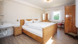 A bedroom with a wooden bed, a bedside table, a nightstand, a wooden wardrobe, a window with curtains, and a radiator. - Vacation apartment "3 Seen" with garden, near Illmensee and Lake Constance (Illmensee)