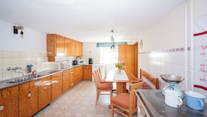 A kitchen with wooden cabinets, a tiled backsplash, a dining table with chairs, and a window with curtains. - Vacation apartment "3 Seen" with garden, near Illmensee and Lake Constance (Illmensee)