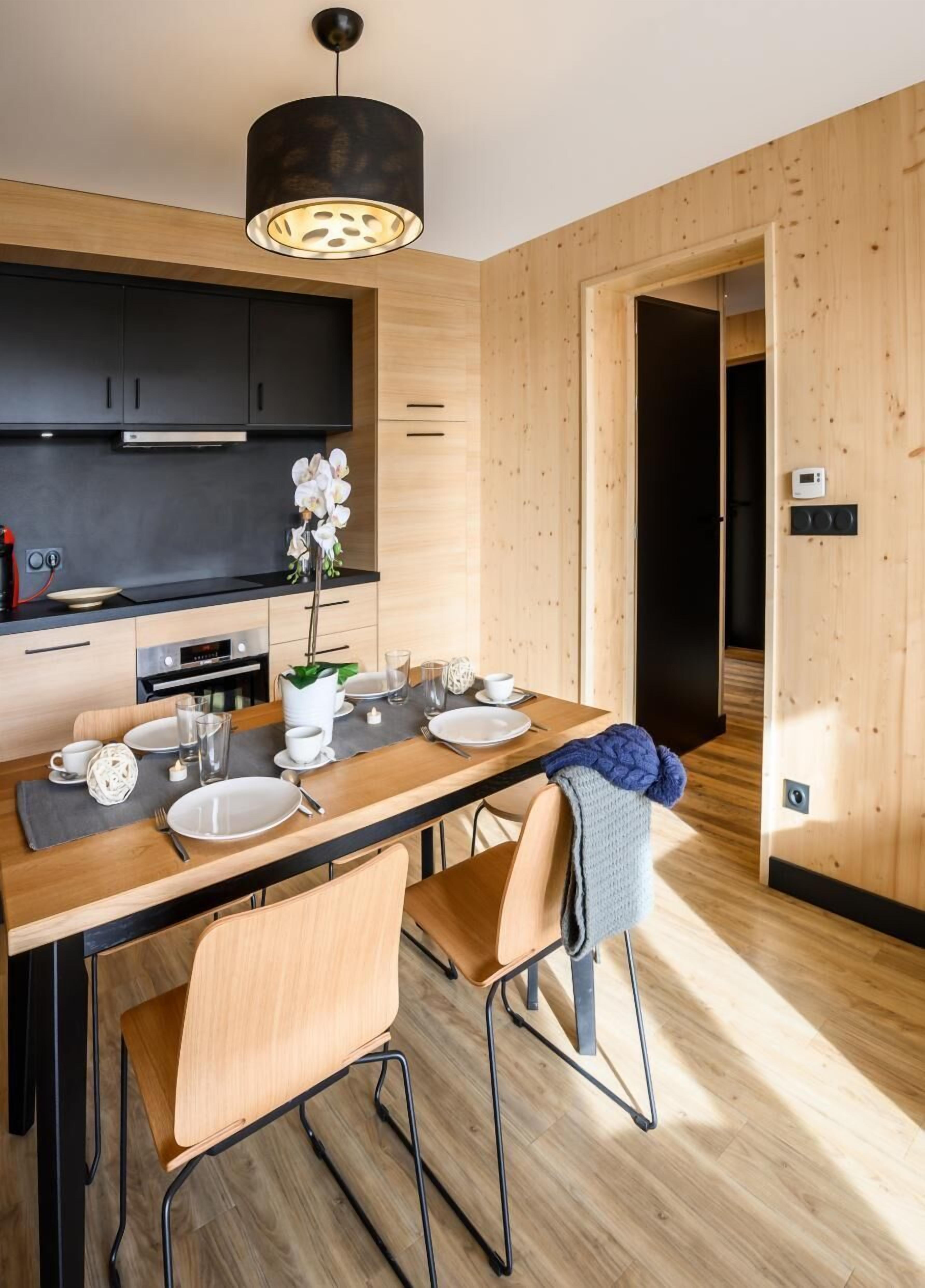 A modern kitchen with dark cabinets, a wooden dining table set for four, and a pendant light above.
