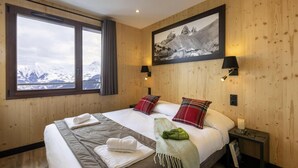 A hotel room with a large bed, two bedside lamps, a framed picture on the wall, and a window with a view of snow-capped mountains. - Wifi, 50m from resort center, swimming pool, terrace, balcony, tv, ski locker, 52m², Le Corbier (Le Corbier)