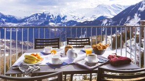 Un coin petit-déjeuner aménagé sur un balcon avec vue sur la montagne, comprenant une table avec des aliments pour le petit-déjeuner et des chaises.