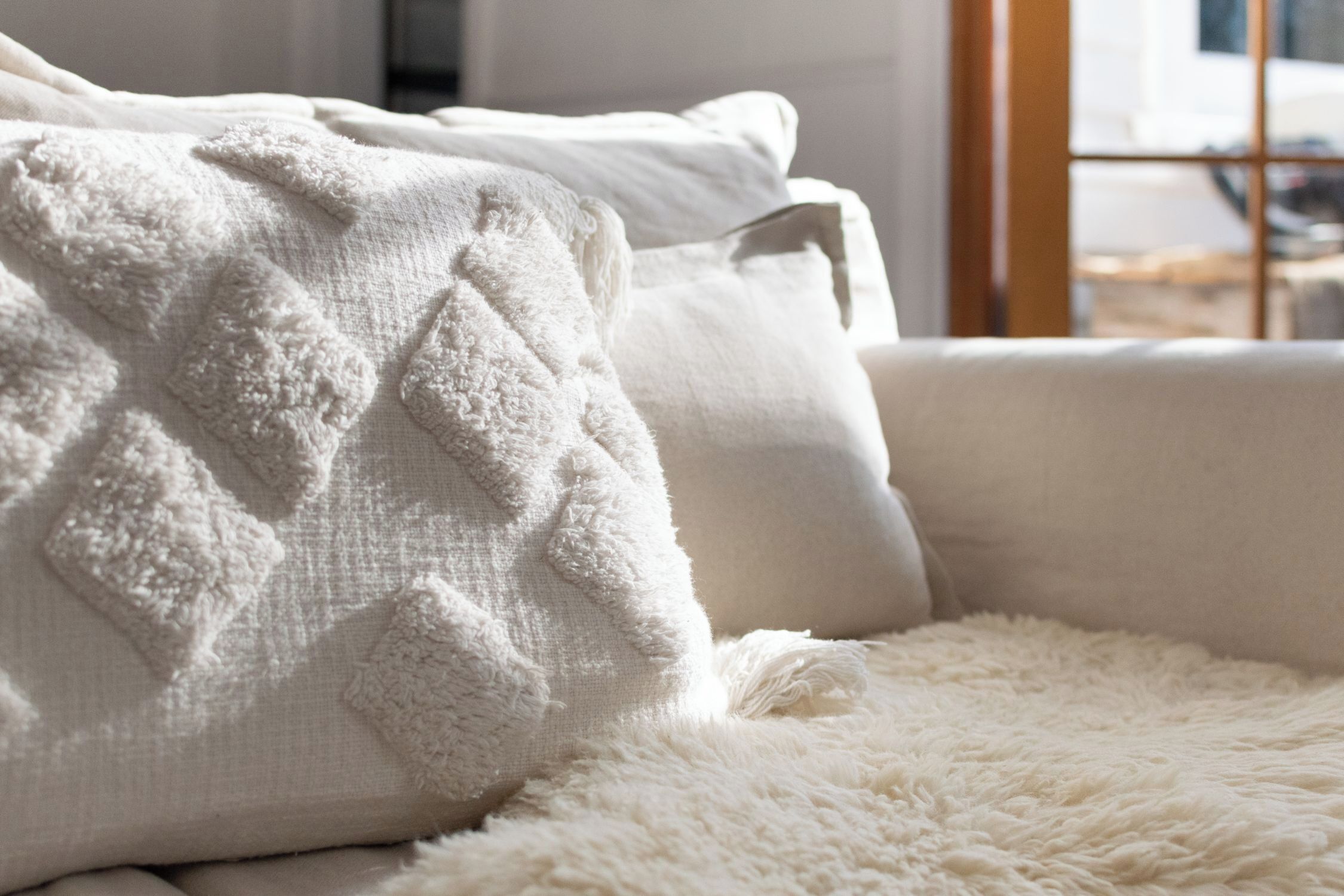 A white sofa with a textured throw blanket and a fluffy white rug.