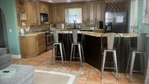 A modern kitchen with wooden cabinets, a granite countertop, stainless steel appliances, and bar stools.