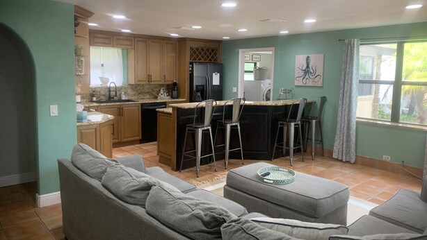 A modern kitchen with a central island, bar stools, and a dining area with a grey sofa.