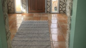 A stone-walled entrance with a wooden door, a ceiling fan, and a patterned rug on tiled flooring.