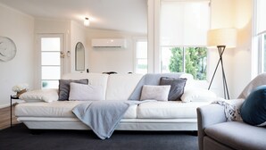 Uma sala de estar moderna com um sofá, uma mesa lateral com luminária e uma janela grande que oferece luz natural.