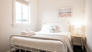 Uma cama bem arrumada com travesseiro, uma mesa de cabeceira com abajur e um quadro na parede.