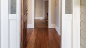 Un couloir au plancher de bois, agrémenté d’un lustre, de moulures blanches et d’une porte dotée d’une poignée en laiton.