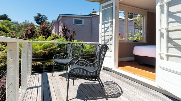 Une terrasse en bois avec des chaises en osier, un lit et une vue sur une maison.