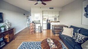 A modern living room with a dark leather sofa, a wooden coffee table, and a patterned rug. A ceiling fan is visible above. - Riverfront balcony  WSR #10 (Wilmington)