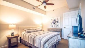 A bedroom with a bed, bedside lamps, a ceiling fan, a dresser, a door, and a wall-mounted TV. - Riverfront balcony  WSR #10 (Wilmington)