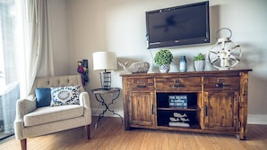 A living room with a sofa, a wooden cabinet, a television, and decorative items. - Riverfront balcony  WSR #10 (Wilmington)