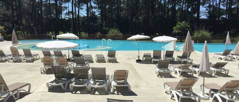 A poolside area with lounge chairs and umbrellas, surrounded by trees.