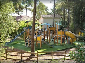 A playground with slides and climbing structures surrounded by trees and a wooden fence. - Nice house in residence with large swimming pool (Lacanau)